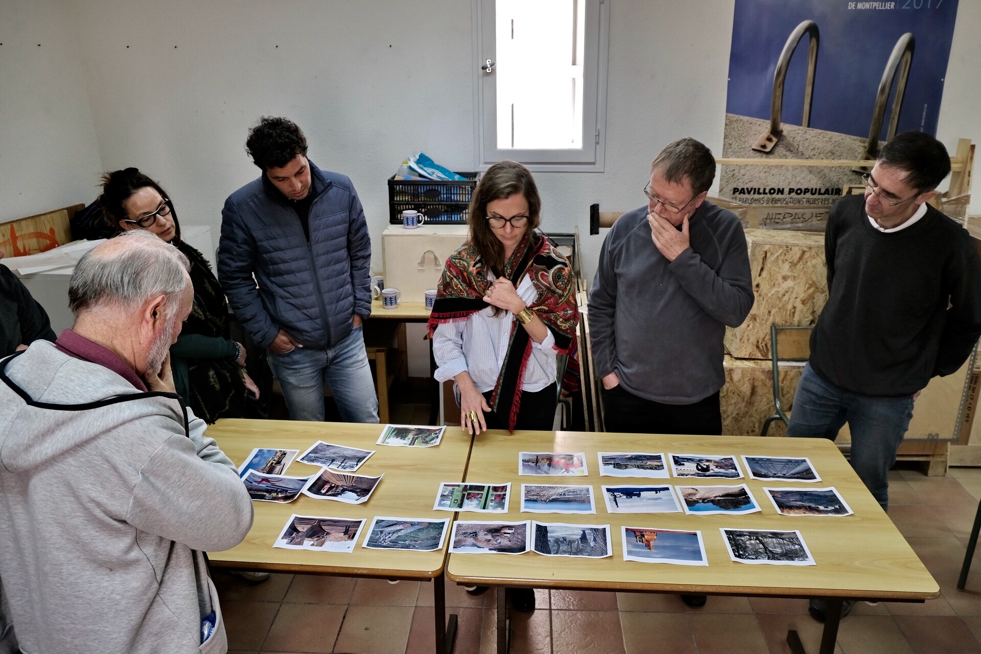 Andrea Olga Mantovani lors d'un workshop de photographie, entourée de stagiaires examinant des tirages photographiques posés sur une table. L'ambiance est studieuse et créative.
